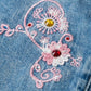 Embroidered floral design on denim fabric with pink and white flowers and red gemstones.