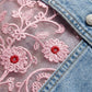 Close-up of pink floral embroidery on a denim fabric background
