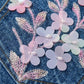 Embroidered floral design on denim fabric with pink and white flowers.