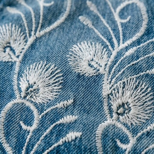 Close-up of blue denim fabric with white floral embroidery