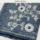 Close-up of denim fabric with floral embroidery and blue stones.