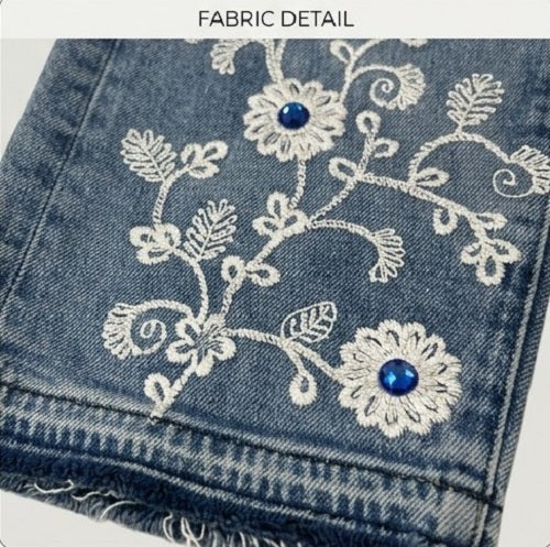 Close-up of denim fabric with floral embroidery and blue stones.