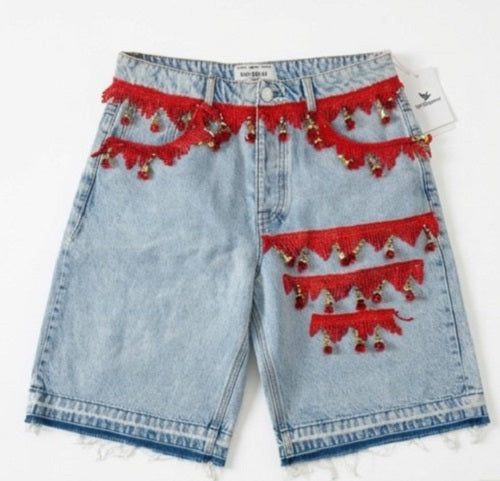 Denim shorts with red fringe and tassel details on a white background