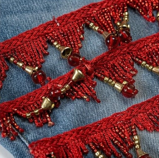 Close-up of red embroidered fabric with gold beads on a blue denim background