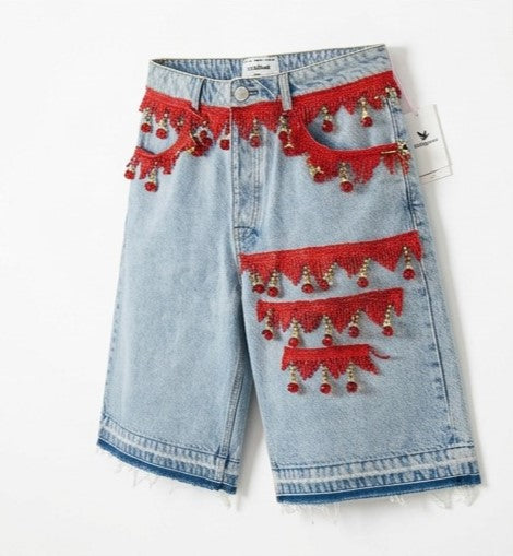 Denim shorts with red lace and bead embellishments on a white background